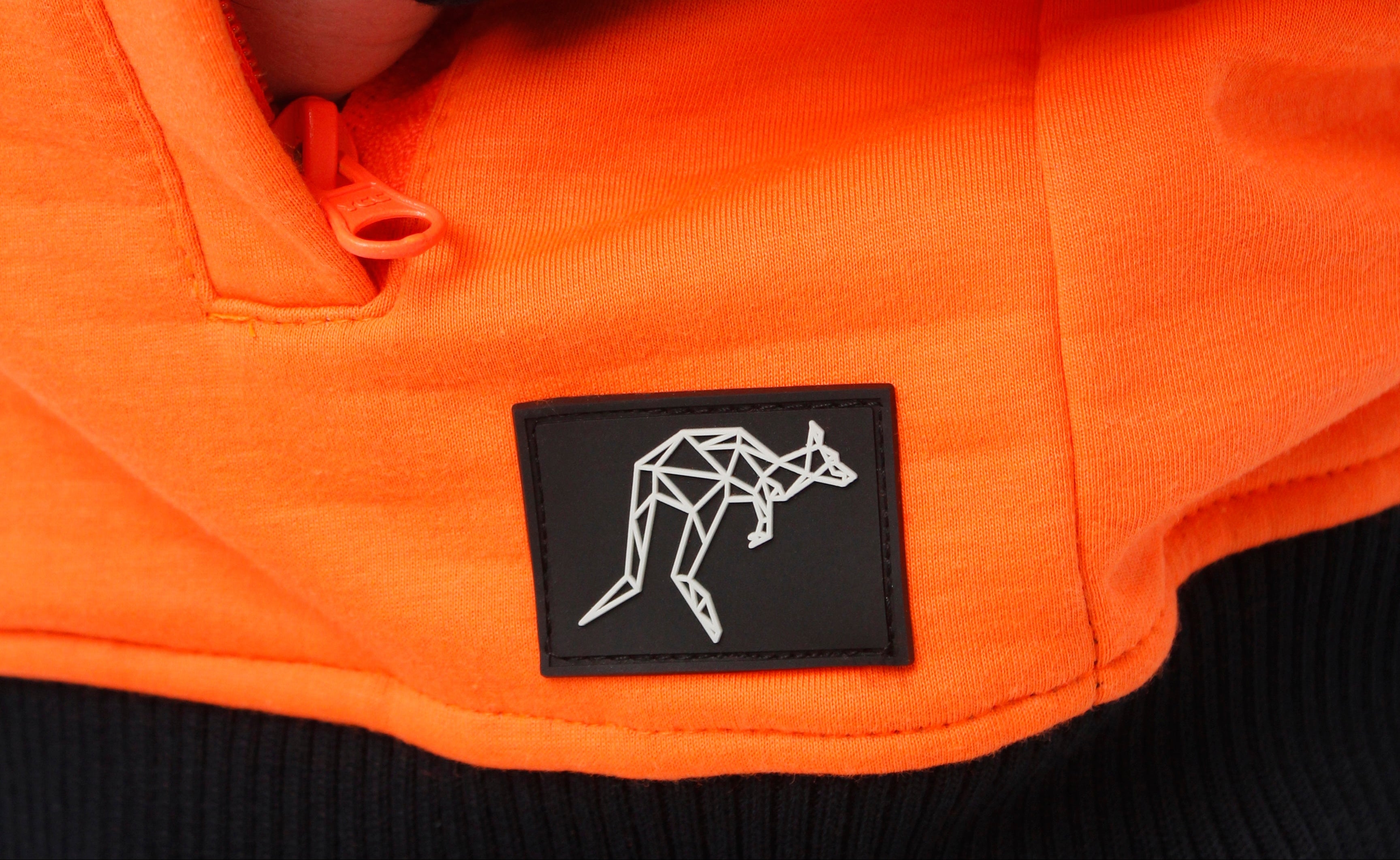 Close-up of an orange jacket with a black patch featuring a geometric kangaroo design.